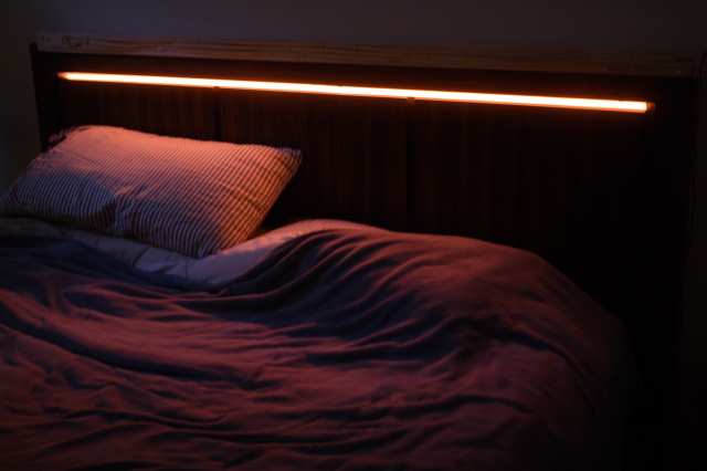 LED lights in bedroom headboard, shining red light downward onto a pair of pillows